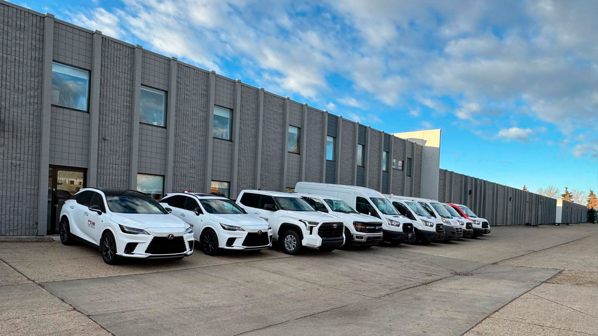 Row of white vehicles, some with CRS Edmonton decals, parked outside a commercial building